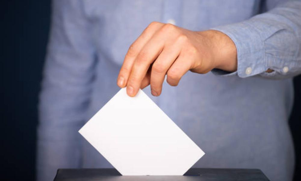 Hand of a voter putting vote in the ballot box.